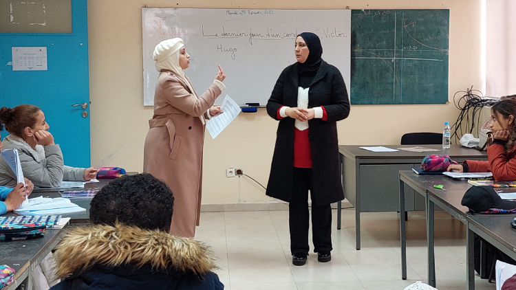 Veiled teacher in a classroom observing her student speaking sign language.