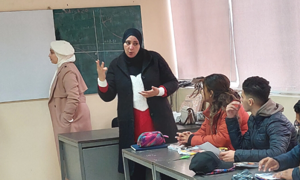 Veiled woman speaking in sign language to high school students in a classroom.